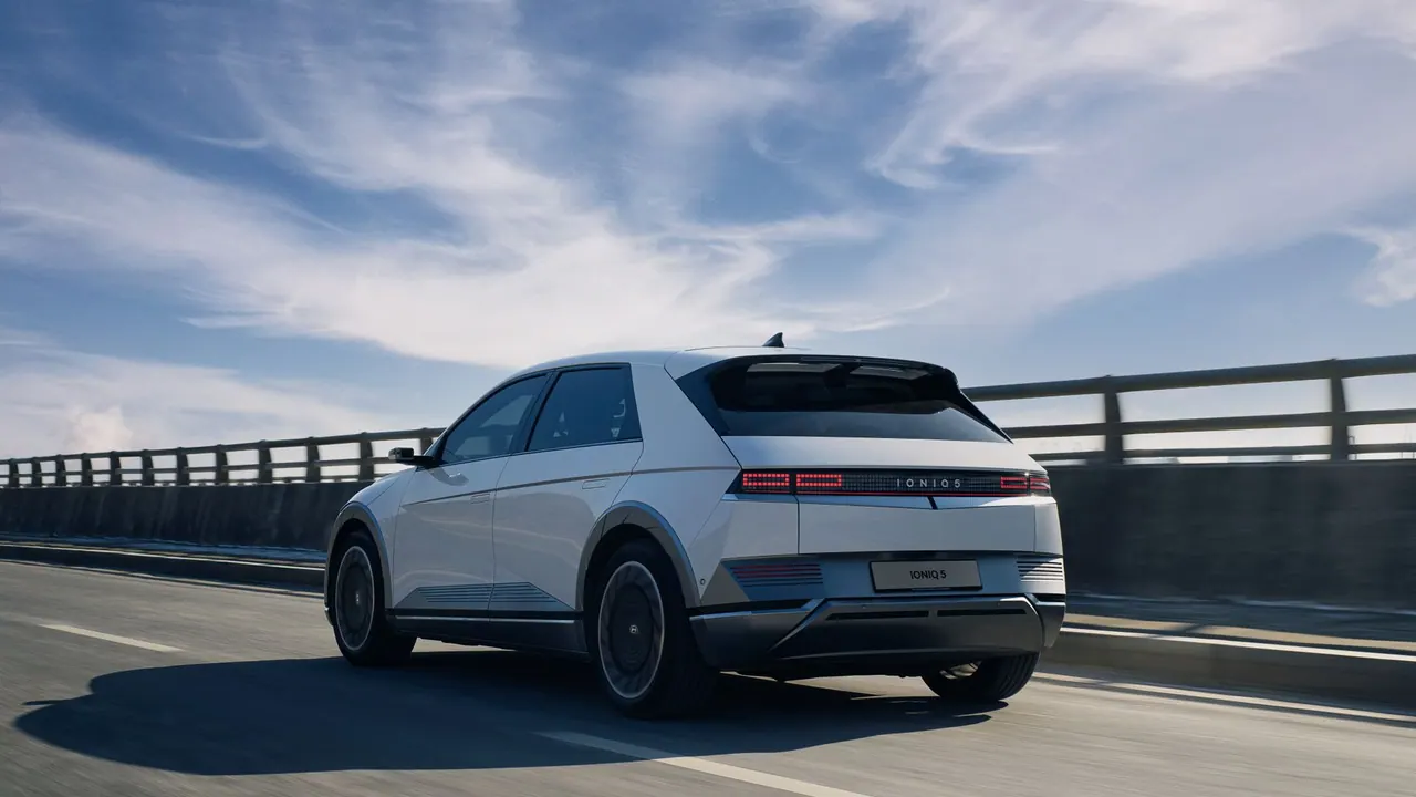 White electric car driving along an open highway beneath a blue sky