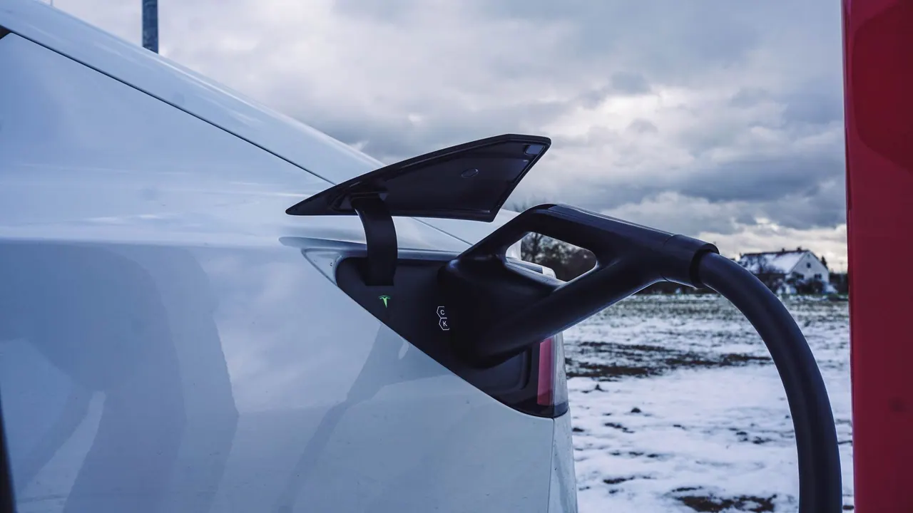 White electric car plugged into a charger in a snowy landscape